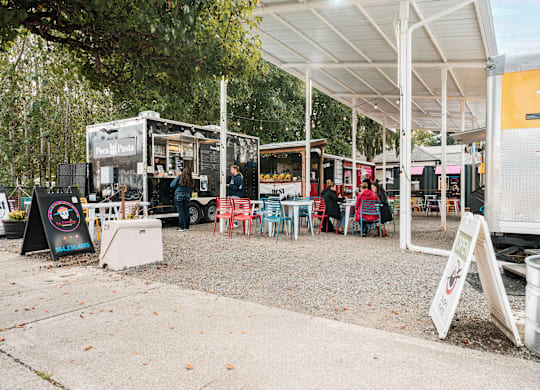A food truck is parked under a white canopy with several people seated at tables outside.
