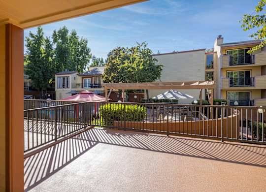 A balcony with a railing overlooks a courtyard with a building and trees.
