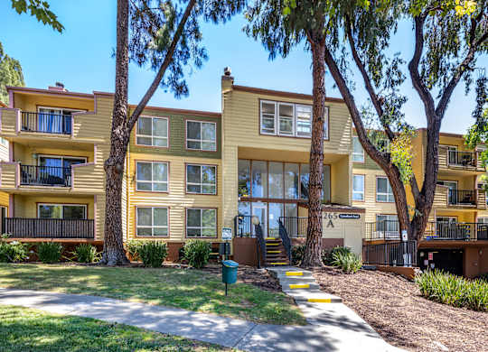 A yellow apartment building with a green trash can in front.