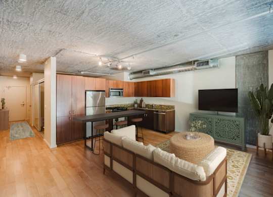 Living room with hardwood floors looking into kitchen featuring stainless steel appliances at at 2121 Belmont apartments in the Buckman neighborhood in Portland, Oregon.