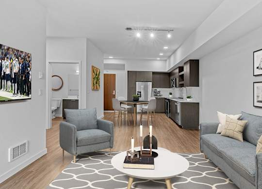 A modern living room with a grey couch, a coffee table, and a dining area in the background.