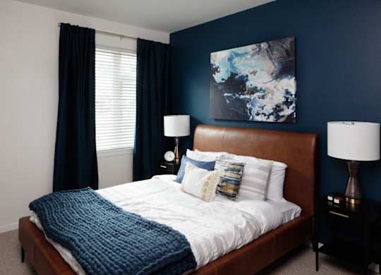 A bed with a white comforter and a blue blanket is in a room with a painting on the wall.