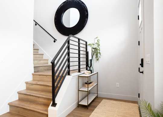 A staircase with a black railing and a round mirror above it.