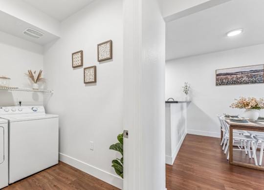 A laundry room with a washer and dryer, a dining table with chairs, and a potted plant.