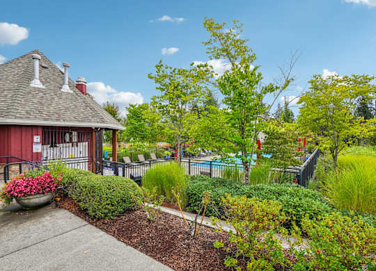 A red building with a grey roof and white chimneys is surrounded by a garden with a variety of plants and trees.