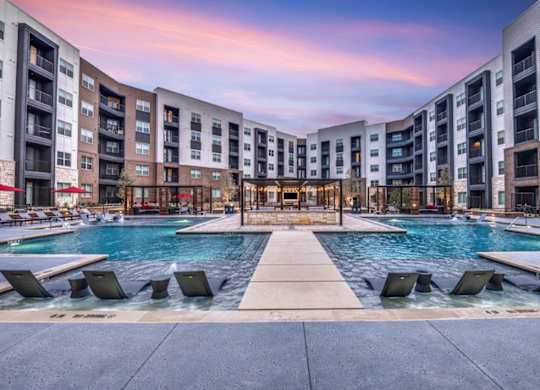 A large outdoor pool surrounded by lounge chairs and buildings.
