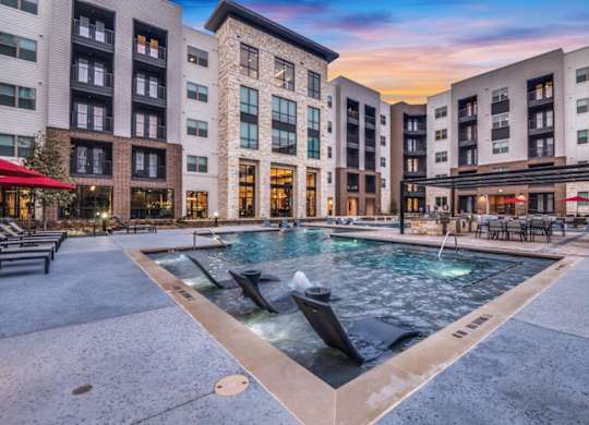 A large outdoor pool surrounded by buildings with a sunset in the background.