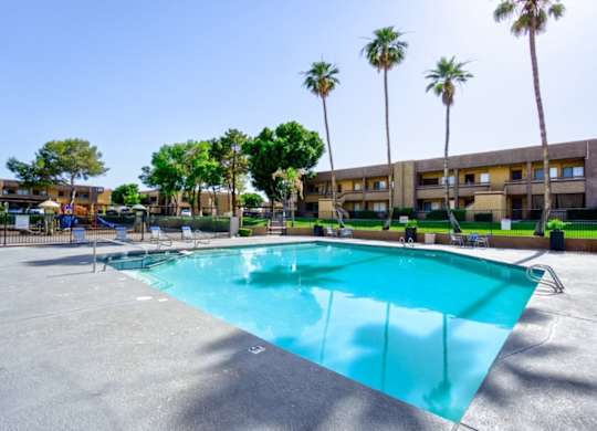 A large swimming pool surrounded by palm trees and apartment buildings.