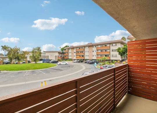 A view from a balcony overlooking a parking lot and apartment buildings.