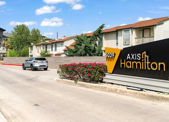 A white car is driving down a street past a building with a sign that says "Axis Hamilton.".