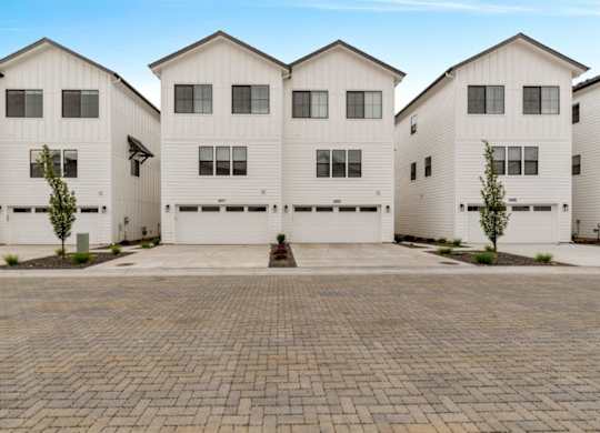 A row of white houses with a brick driveway in front.