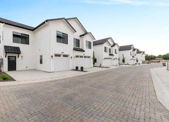 A row of white houses with black roofs and a brick driveway.