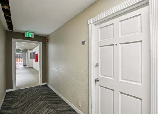 A hallway with a white door and a green exit sign.