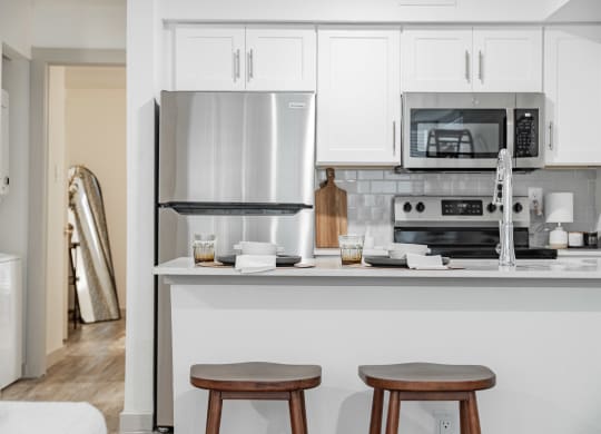 a kitchen with white cabinets and a counter with two stools