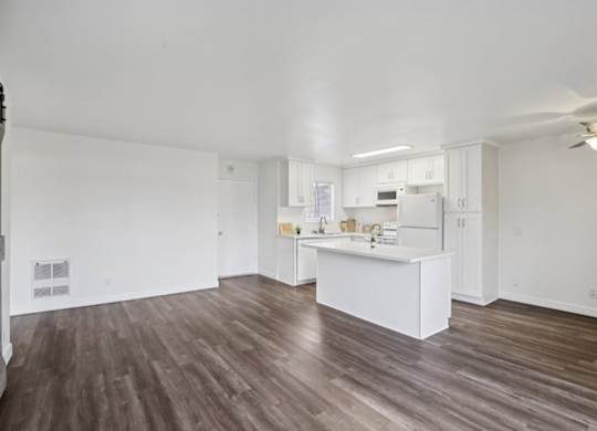 A spacious kitchen with white cabinets and a wooden floor.