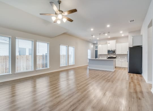 an empty living room with a ceiling fan and a kitchen