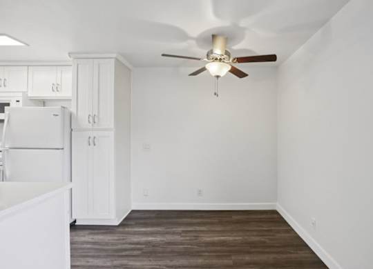 A white kitchen with a ceiling fan and wooden floors.