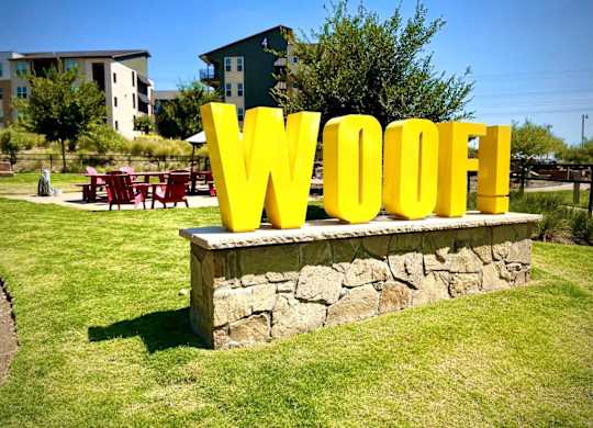 A large yellow Woof! sign is displayed in a grassy area.
