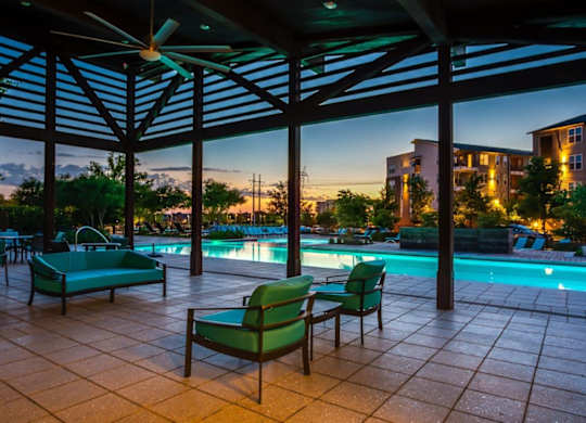 A patio with a pool and chairs under a roof.