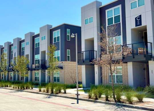 A row of modern apartment buildings with balconies and trees in front.