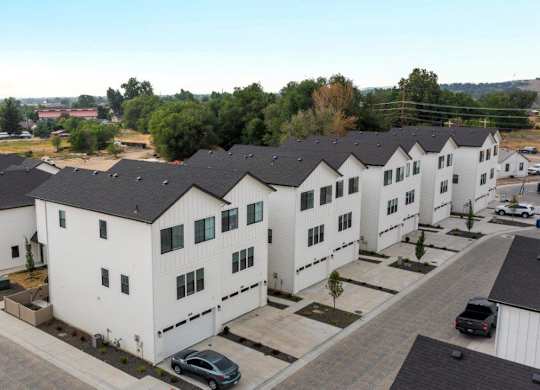 A row of white houses with black roofs and cars parked in front.