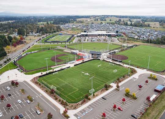 An aerial view of a sports complex with a soccer field, football field, and parking lot.