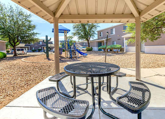A playground with a table and chairs under a canopy.