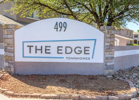 A sign for "The Edge" townhomes stands in front of a building.
