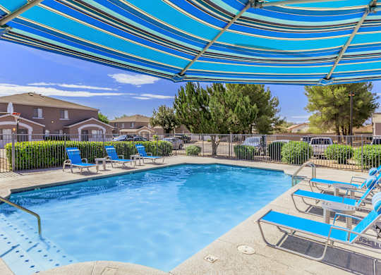 A pool with a blue canopy and lounge chairs.