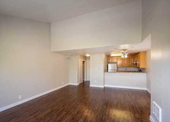 A large empty room with wooden floors and a kitchen area in the background.