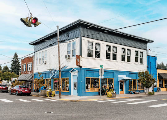 A cyclist is crossing the street in front of a blue building.
