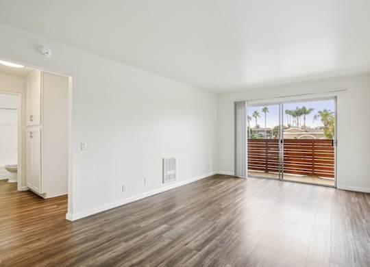 A room with wooden floors and a sliding glass door leading to a balcony.