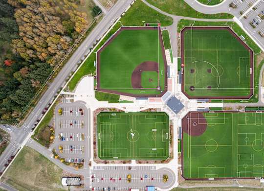An aerial view of a sports complex with a baseball diamond, soccer fields, and a parking lot.