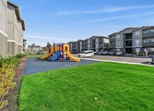 A playground with a blue and yellow slide in the foreground and apartment buildings in the background.