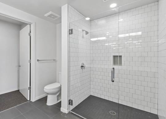 A white tiled bathroom with a toilet and a walk-in shower.