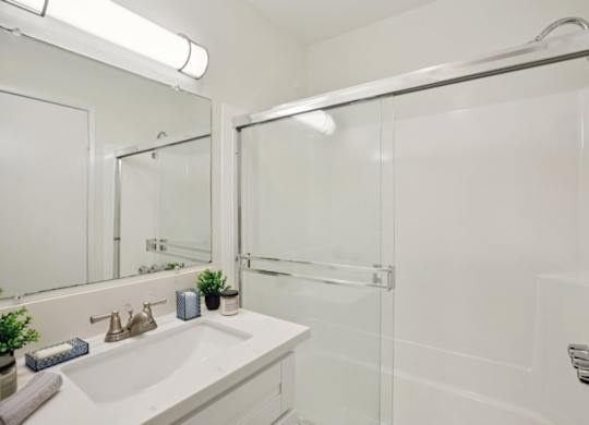 A white bathroom with a sink, mirror, and shower.