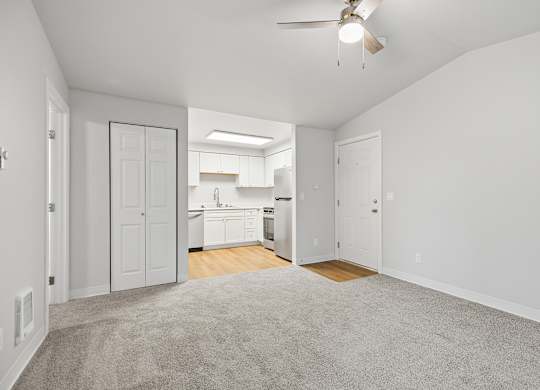 A spacious, empty room with a carpeted floor and a ceiling fan.