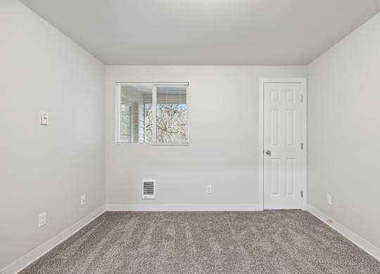 A room with a carpeted floor and a window with blinds.