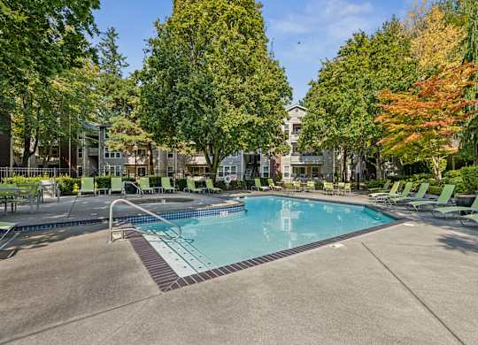 A swimming pool surrounded by trees and lounge chairs.