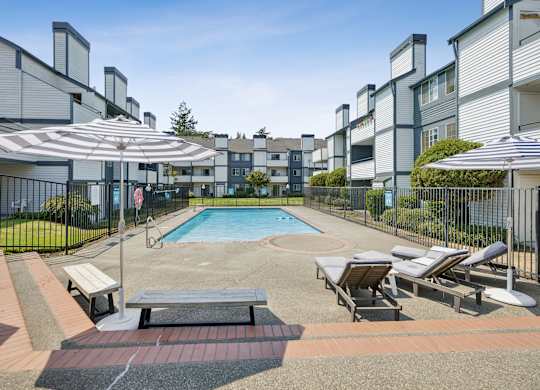 A pool surrounded by lounge chairs and umbrellas in a residential area.