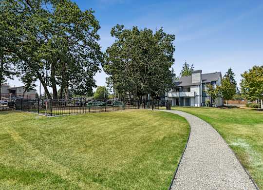 A gravel path leads through a grassy area with trees and a building in the background.