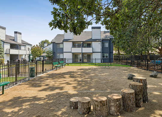 A playground area with a large tree stump in the center and a building in the background.