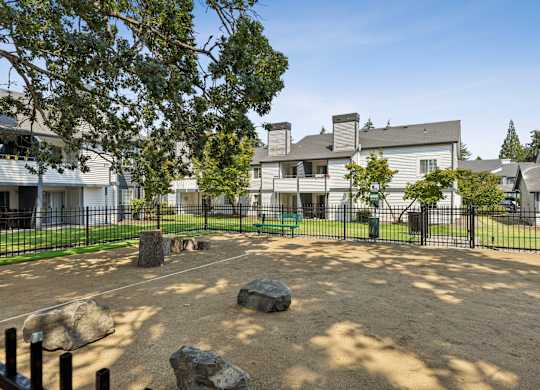 A playground area with a sandbox and rocks in the foreground and a building in the background.