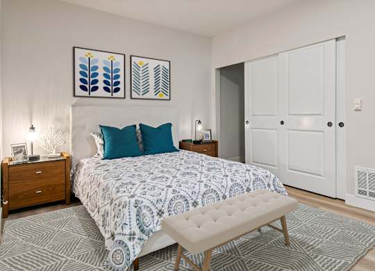 A bedroom with a patterned bedspread and a bench in front of it.