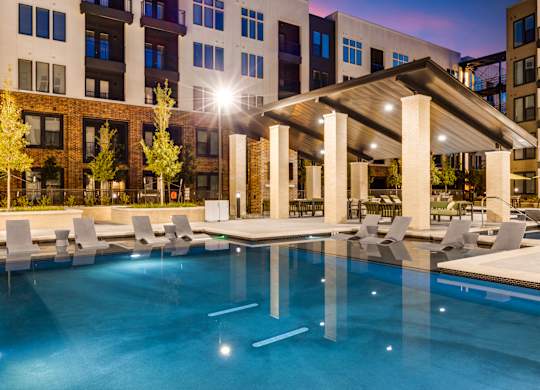 A swimming pool with a pavilion and chairs in front of apartment buildings.