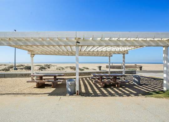 A white beach shelter with a metal roof is in the foreground with a beach in the background.