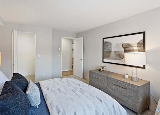 A bedroom with a bed, nightstand, and a painting on the wall.