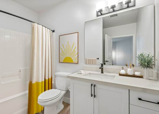 A bathroom with a white toilet, sink, and a yellow shower curtain.