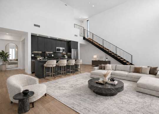 A modern living room with a staircase and a kitchen in the background.