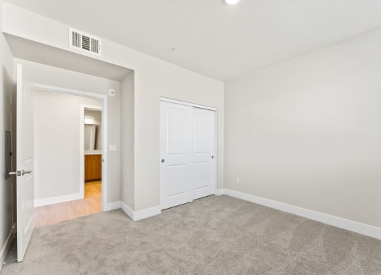 a bedroom with white walls and carpet and a door to a bathroom